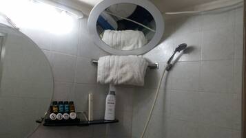 Un baño con un espejo redondo, un perchero con una toalla blanca, un cabezal de ducha y un estante con artículos de aseo.