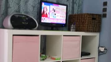 Una habitación con una televisión sobre un mueble bajo, un armario con cajones rosas y una cortina estampada.