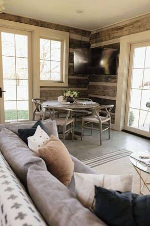 A modern living room with a sofa, dining table, chairs, and a flat-screen TV mounted on a wooden wall.