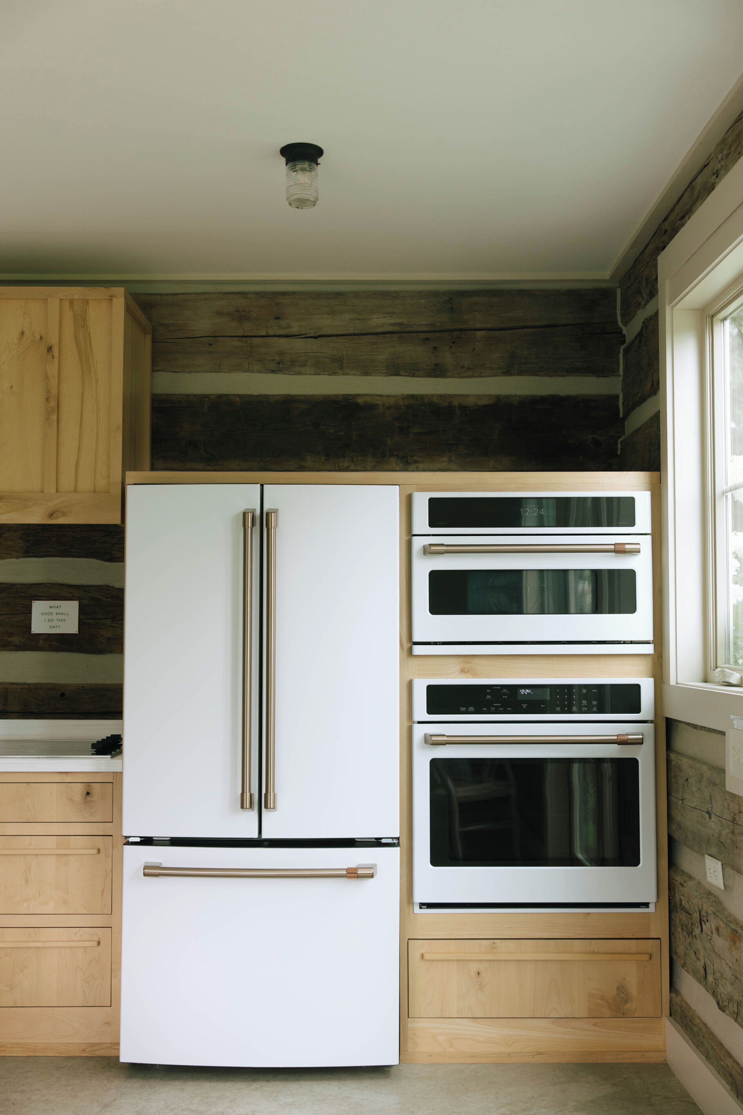 A kitchen with a white refrigerator, two ovens, wooden cabinets, and a window.