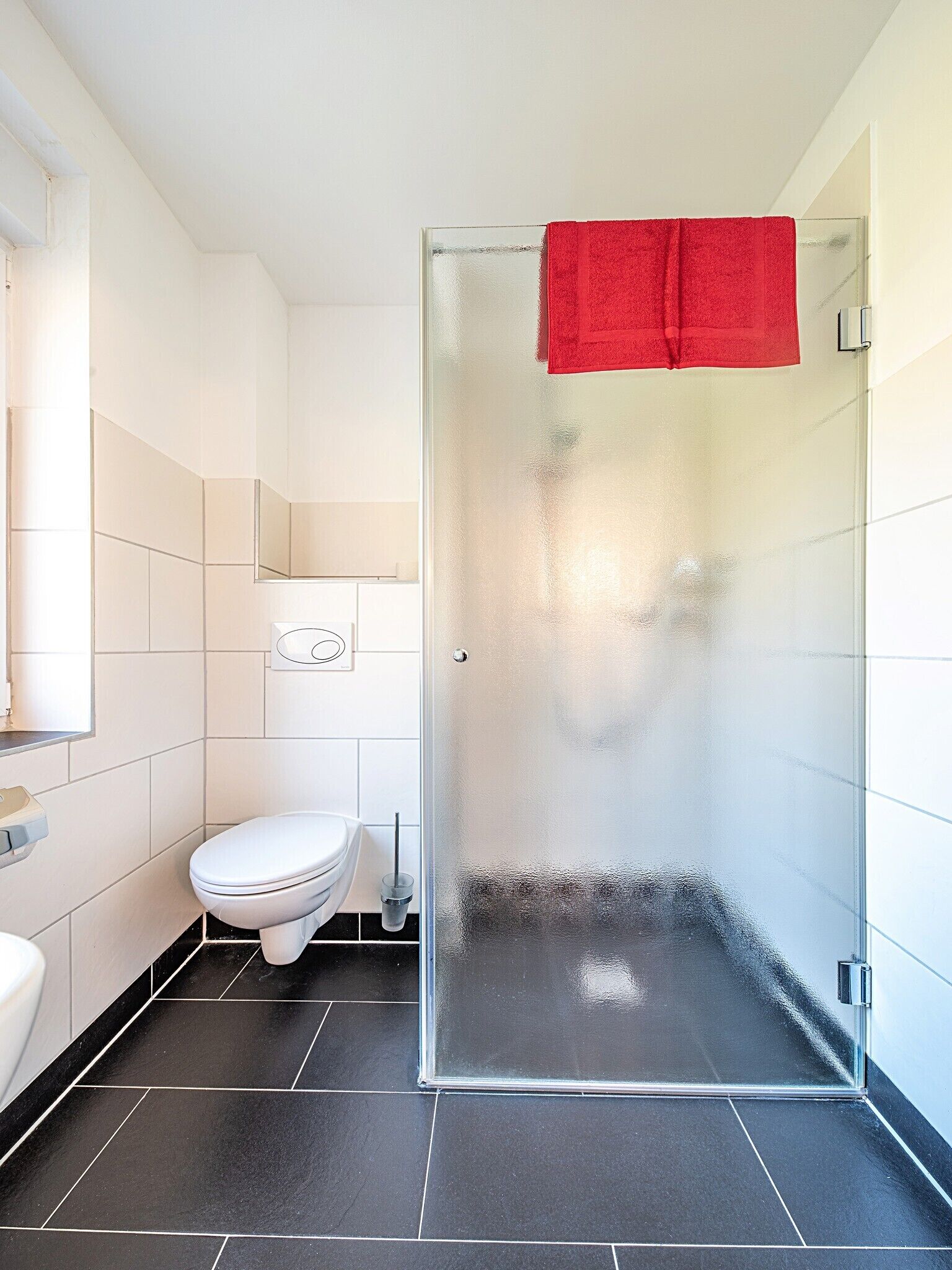 Un baño moderno con ducha envuelta en vidrio, inodoro blanco y espejo sobre el lavabo.