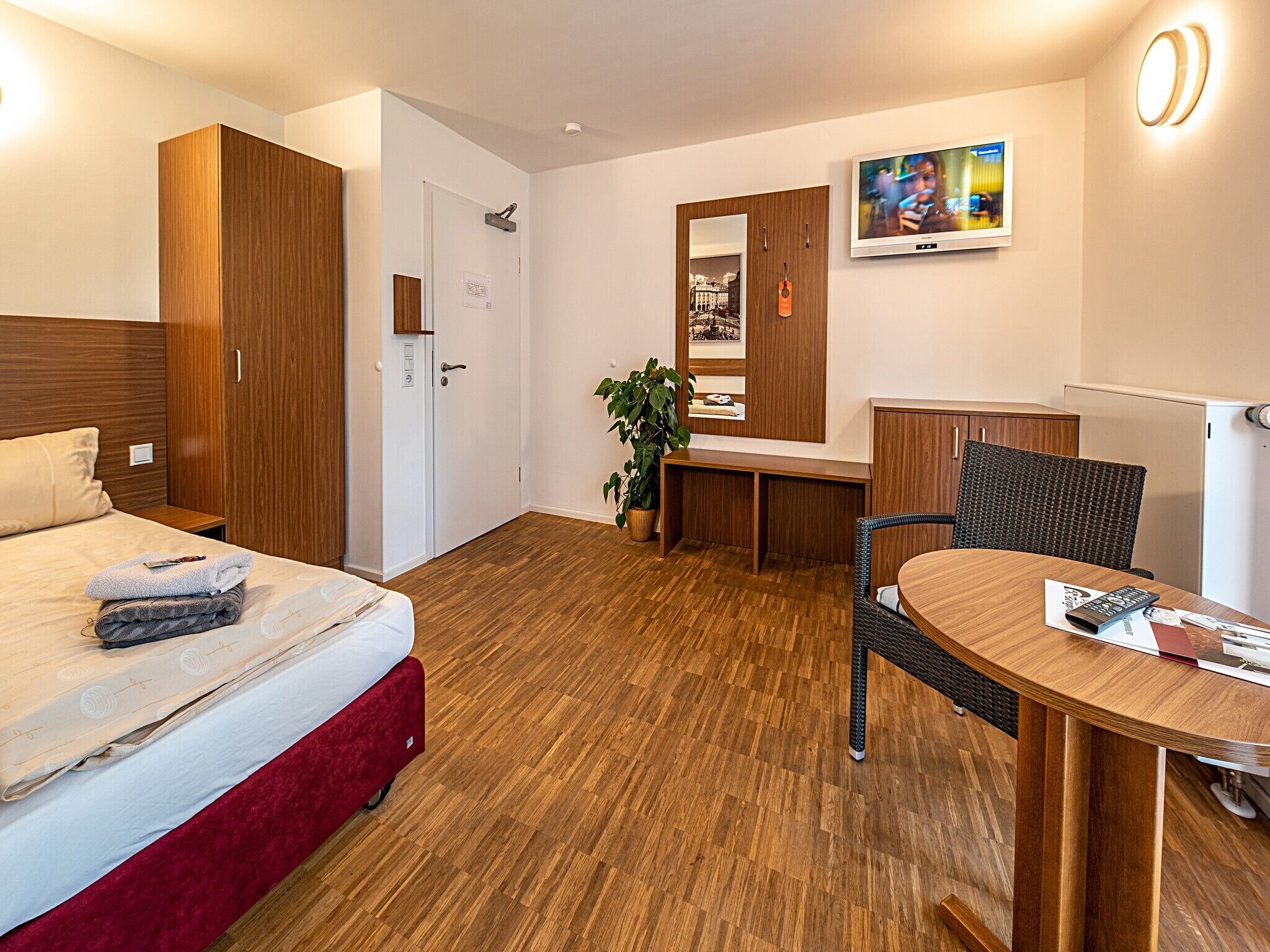 Habitación de hotel con cama, escritorio, silla, televisión y espejo.