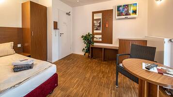 Habitación de hotel con cama, escritorio, silla, televisión y espejo.