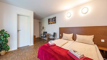 A hotel room with a wooden headboard, a red blanket, and a small desk with a chair.