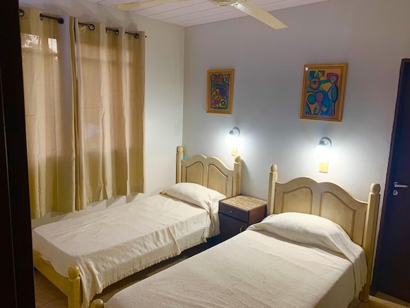 A room with two single beds, a nightstand, a wall-mounted lamp, and a door.