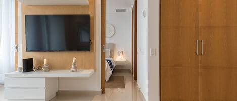 A modern living room with a flat-screen TV mounted on a wooden wall, a white console table with decorative items, and a wooden wardrobe.