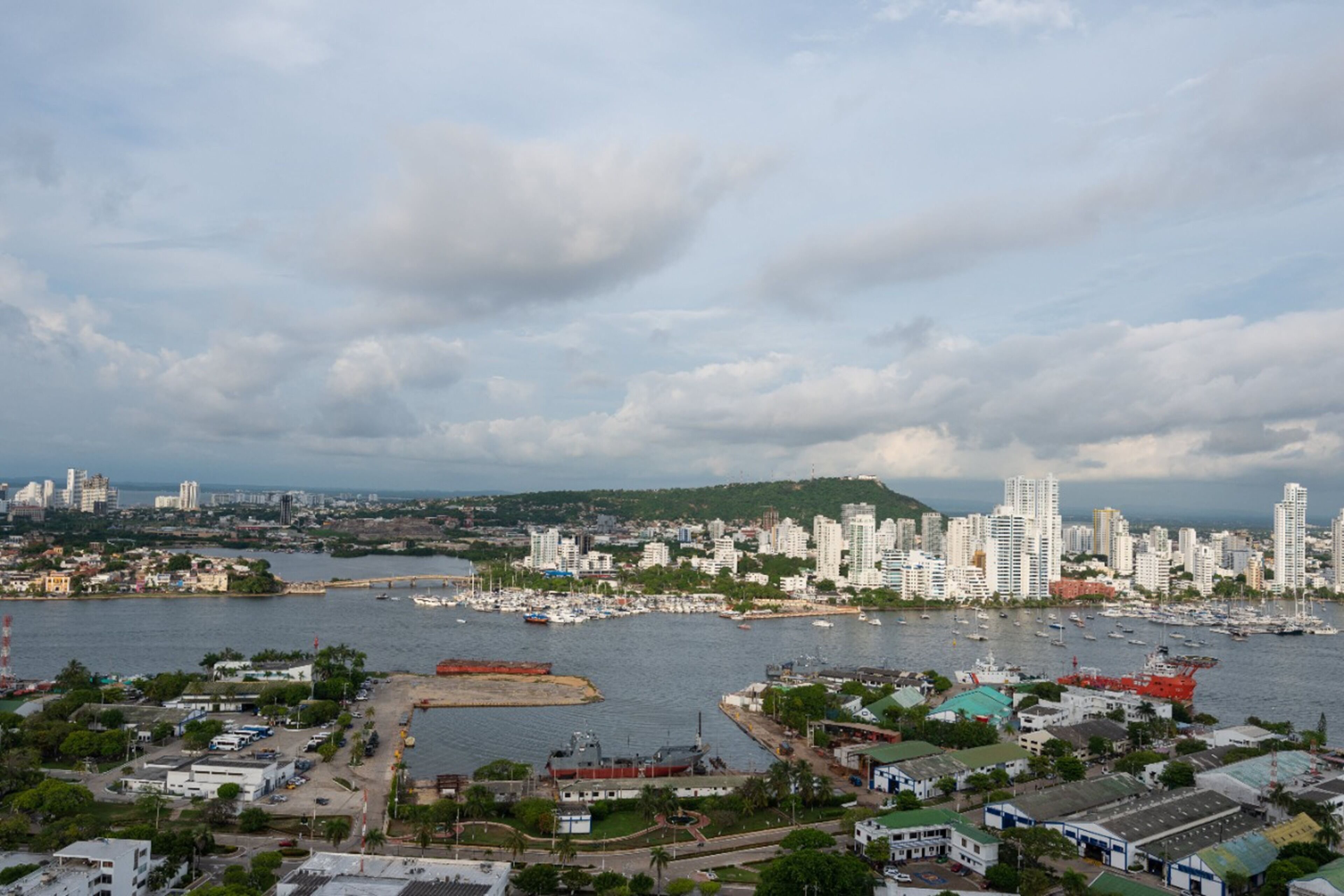 A coastal cityscape with a marina, high-rise buildings, and a hilly background.