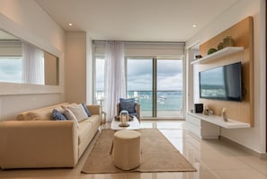 Uma sala de estar moderna com sofá, mesa de centro, puf e televisão na parede.
