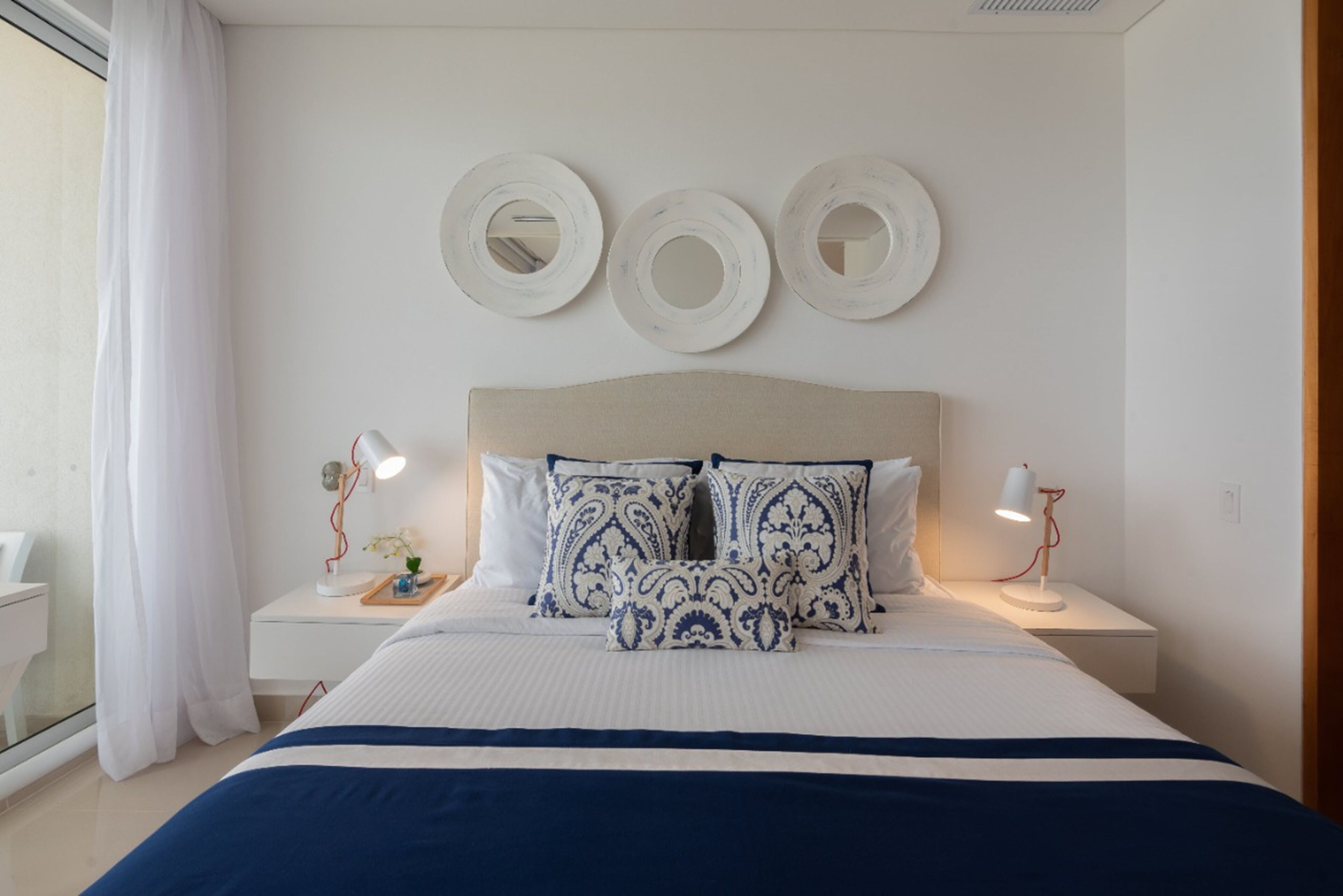 Une chambre à coucher bien aménagée, avec un grand lit, deux tables de chevet et trois miroirs fixés au mur.