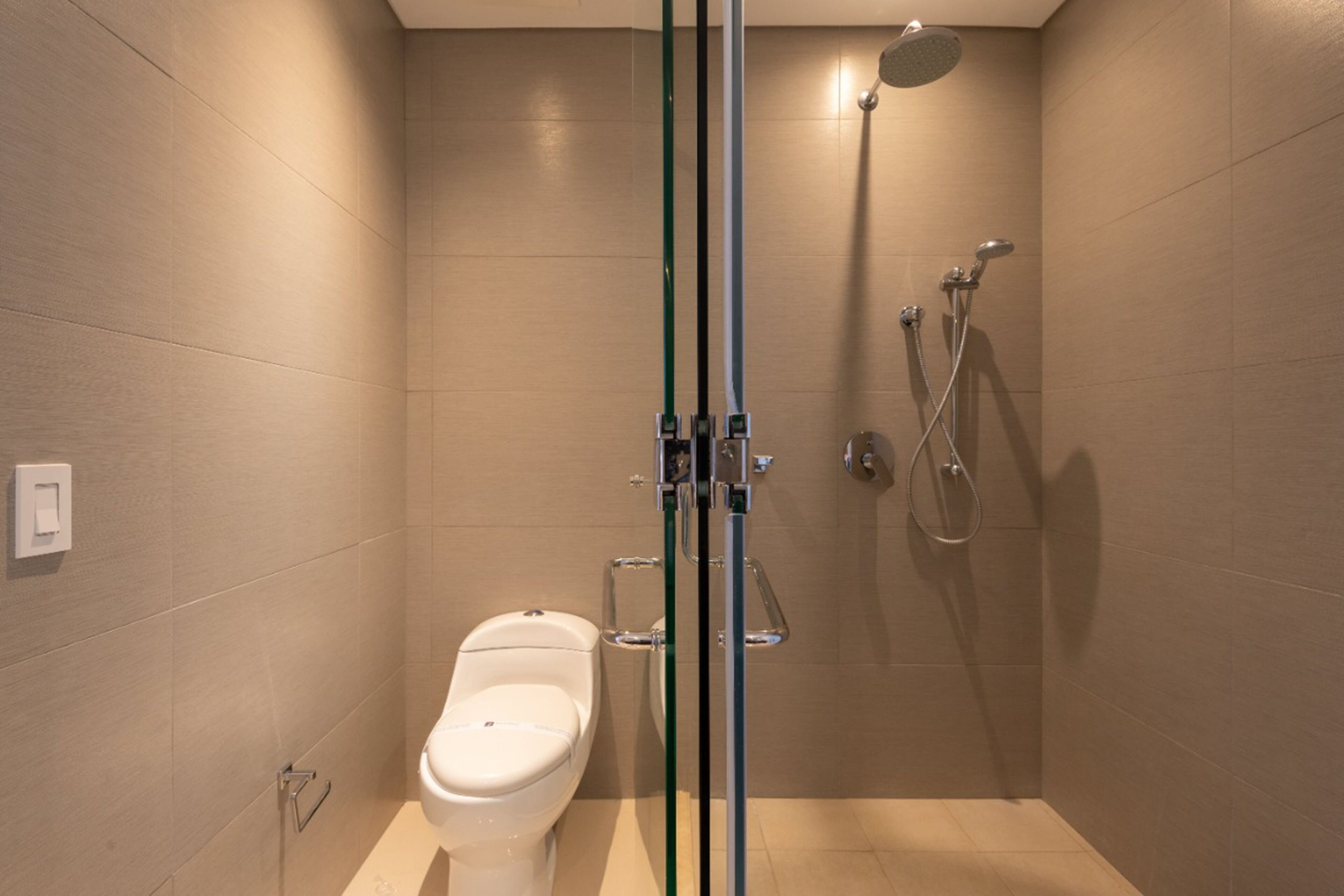 A modern bathroom with a toilet, a shower with a handheld showerhead, and a glass partition.