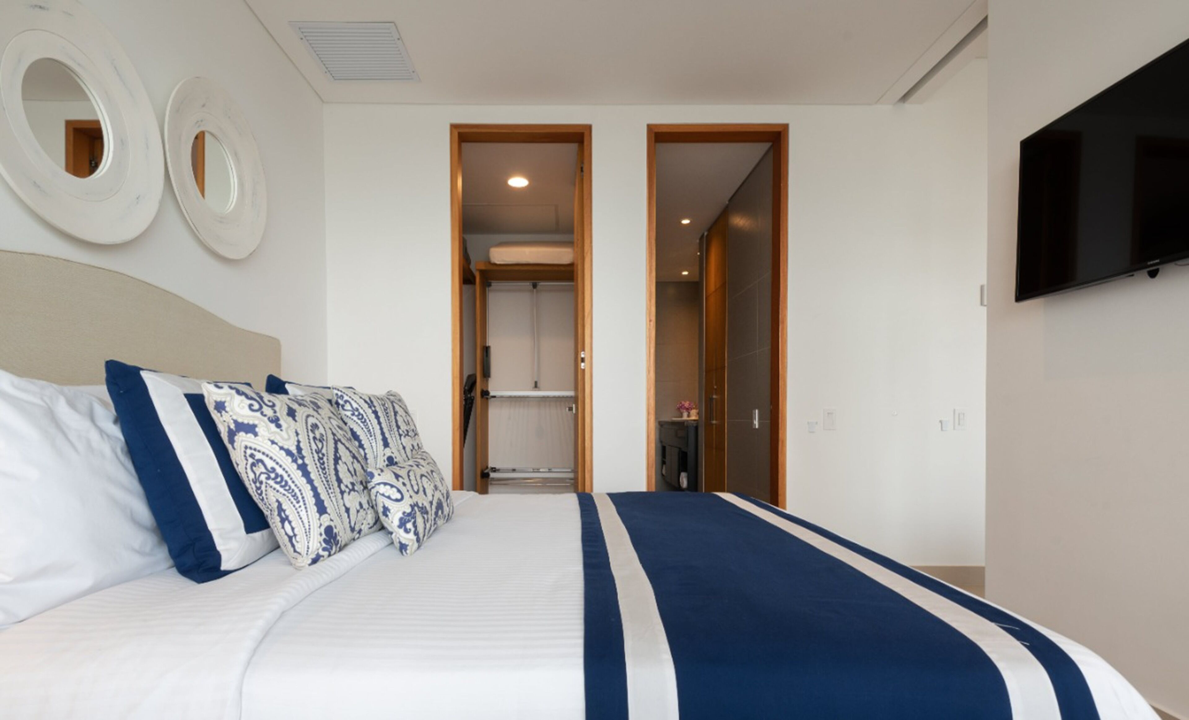 Ein Hotelzimmer mit einem großen Bett, zwei Türen zu einem Badezimmer und einem Schrank, einem an der Wand montierten Fernseher und runden Wanddekorationen.