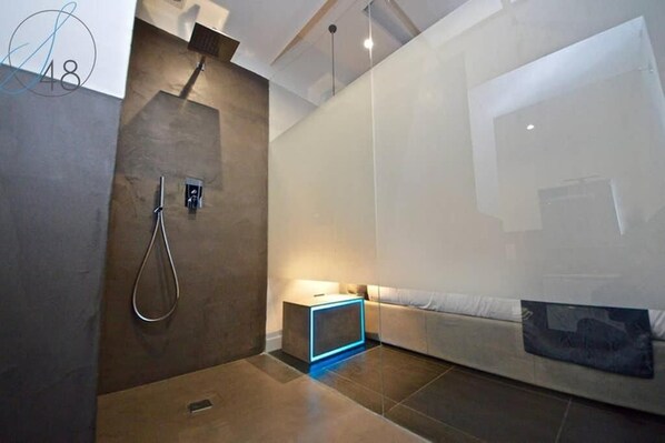 Un baño moderno con ducha, una mesita de noche pequeña y un sofá.
