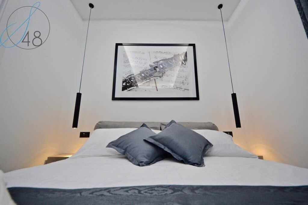 Une chambre moderne avec un lit, deux oreillers, une œuvre d’art encadrée au mur et le chiffre « 48 » dans un coin.
