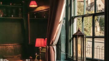 A dimly lit room with a table set for two, a chair, a lamp, and a view of a street through a window.