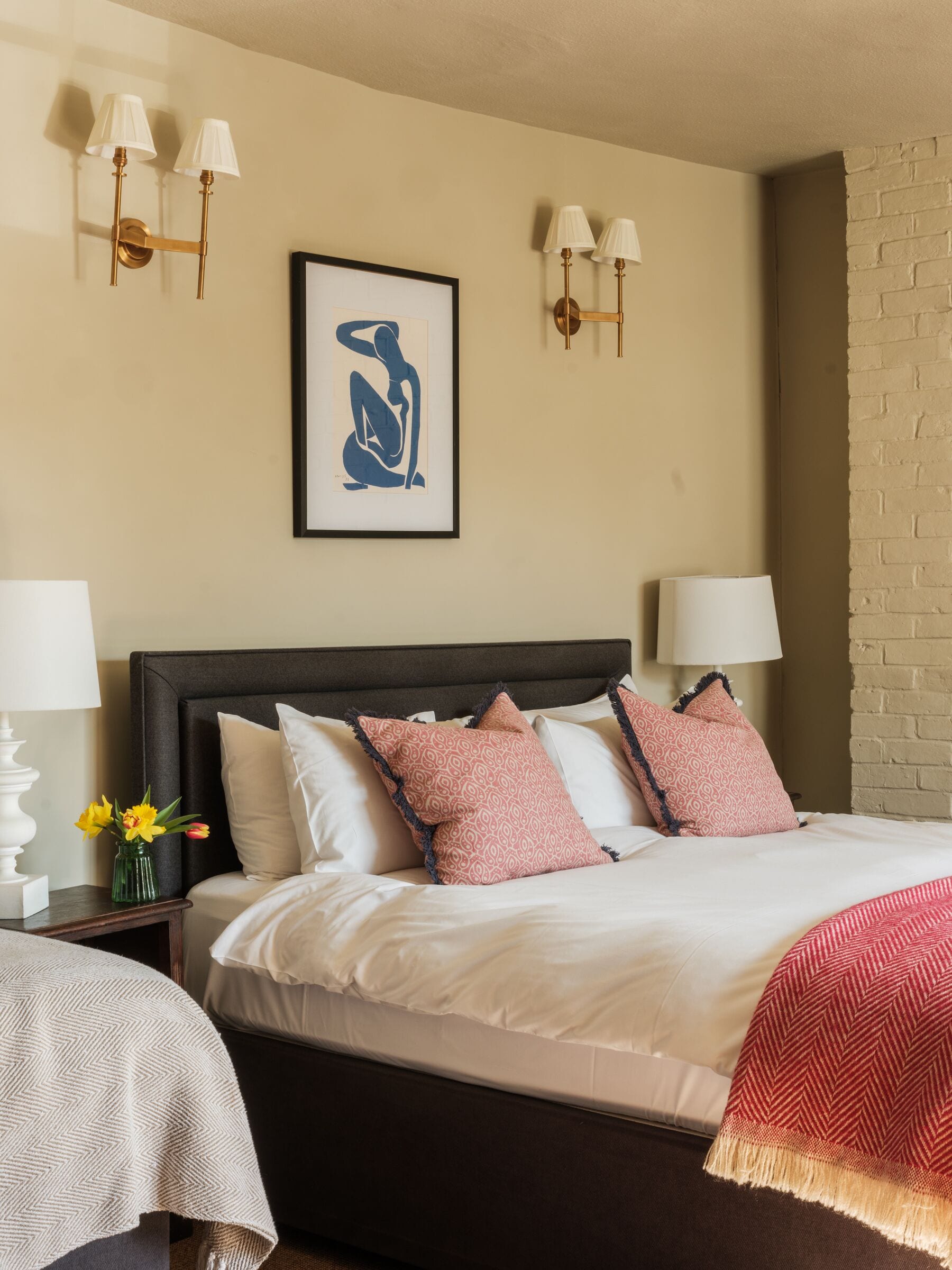 A hotel room with a large bed, two bedside lamps, a framed artwork, and a vase with flowers.