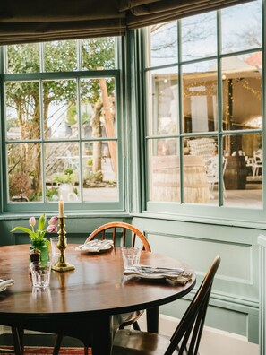 A dining table with chairs, a candle, and a vase with flowers. - The Grosvenor Arms (Salisbury)