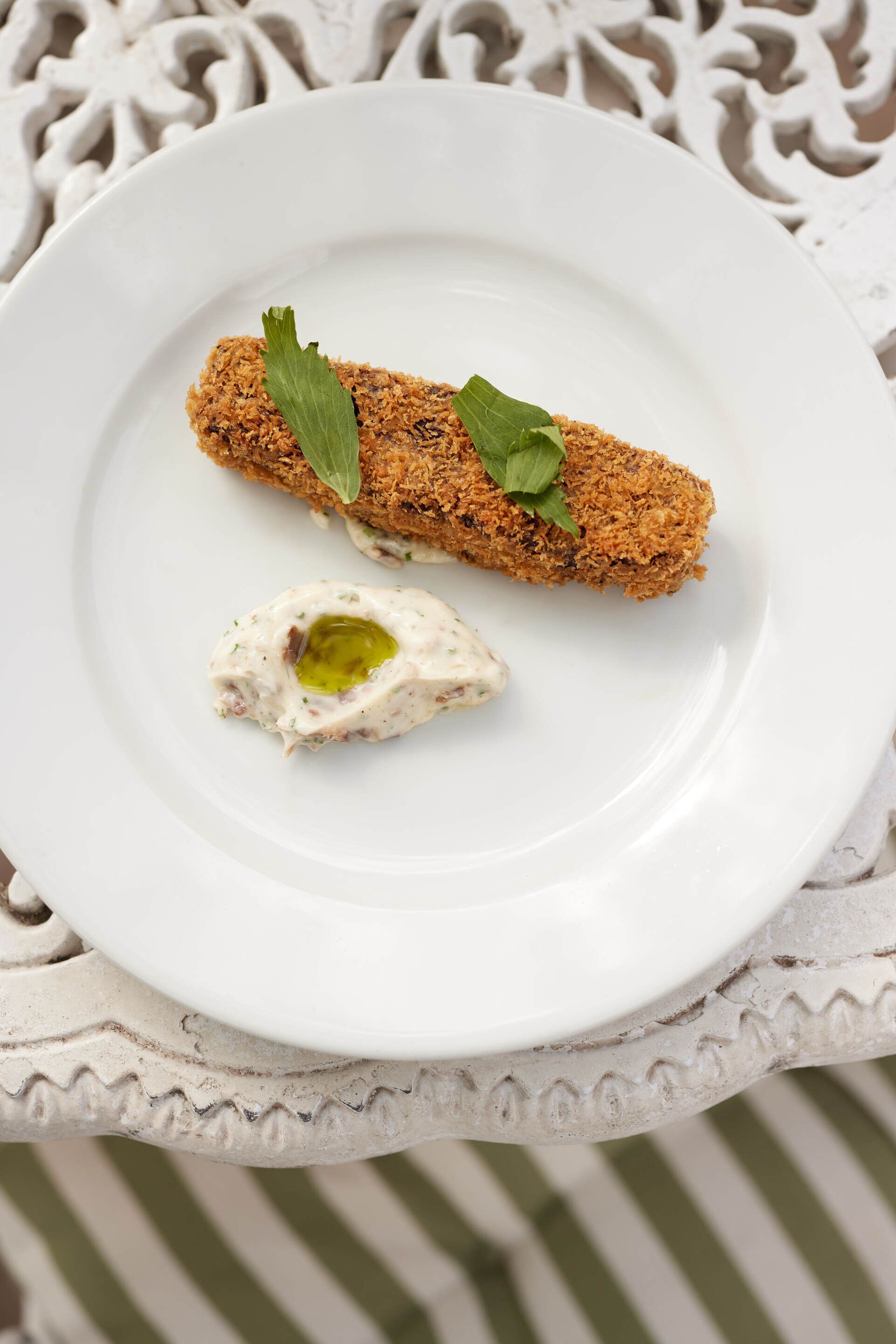 A white plate with a breaded item and a creamy sauce, set on a white ornate table.