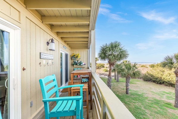 Un balcon avec une table et des chaises en bois, un petit jardin avec des palmiers et une vue dégagée sur la plage.