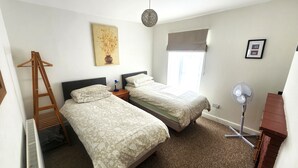 A bedroom with two beds, a wooden ladder, a standing fan, a radiator, and a window with a blind. - 2-bed Flat With Superfast Wi-fi DW Lettings 29br (Sittingbourne)