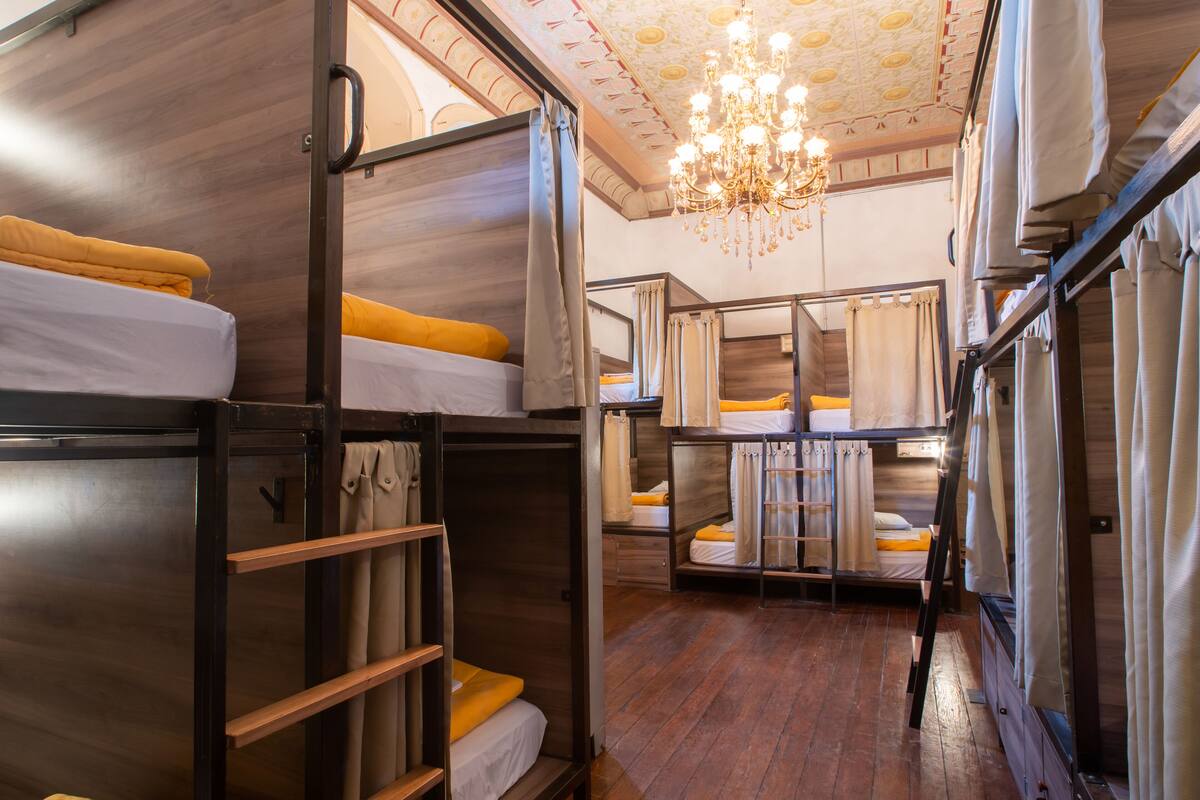 A dormitory room with bunk beds, wooden floors, and a chandelier.