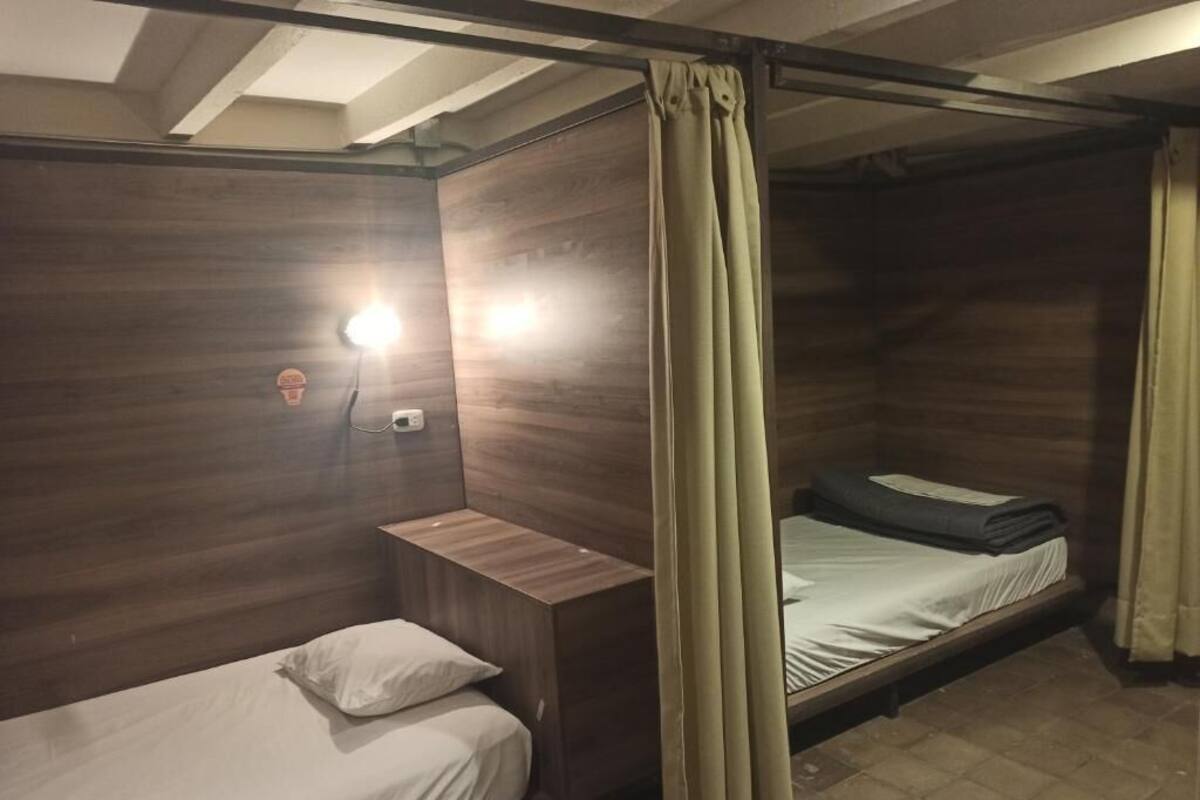 A room with two wooden bunk beds, each with a pillow and a headboard. There is a nightstand with a lamp on the left bed.