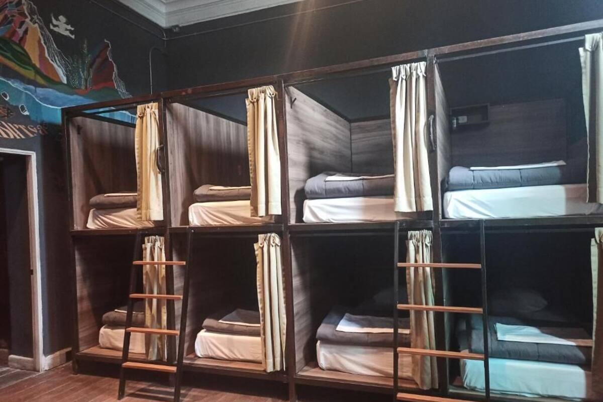A room with bunk beds arranged in two rows, wooden ladders, and curtains.