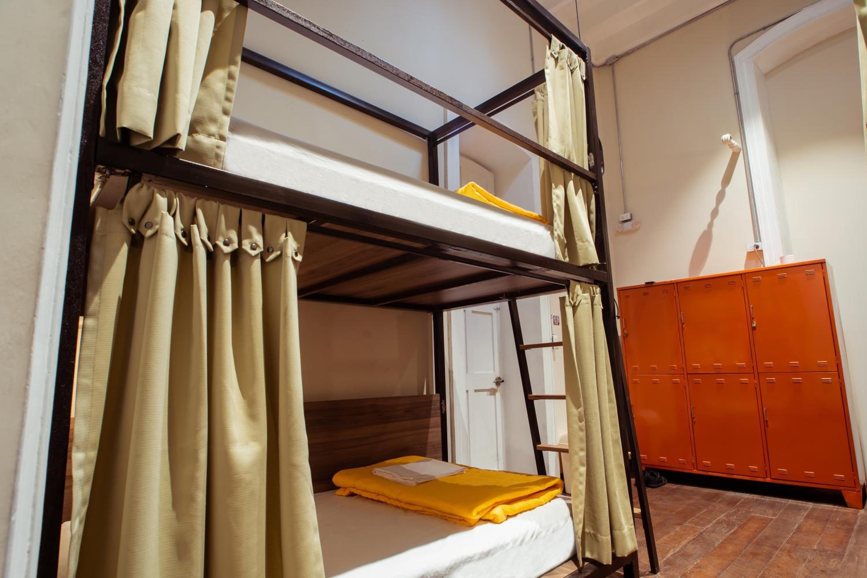 Un lit superposé avec des rideaux, une échelle et des casiers orange dans une pièce dont le sol est carrelé.