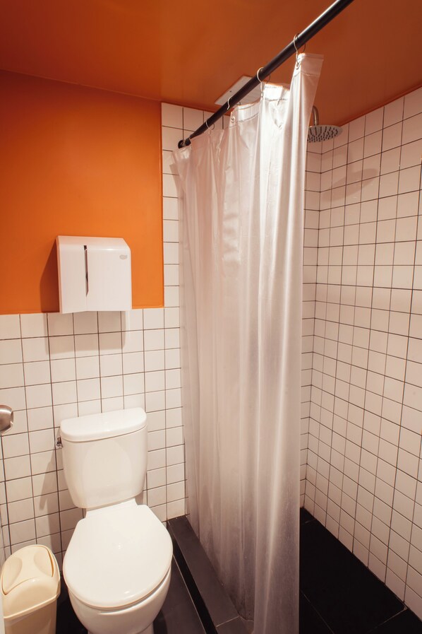A bathroom with a white toilet, a white trash bin, and a shower curtain. - Viajero Lima - Barranco Hostel (Lima)