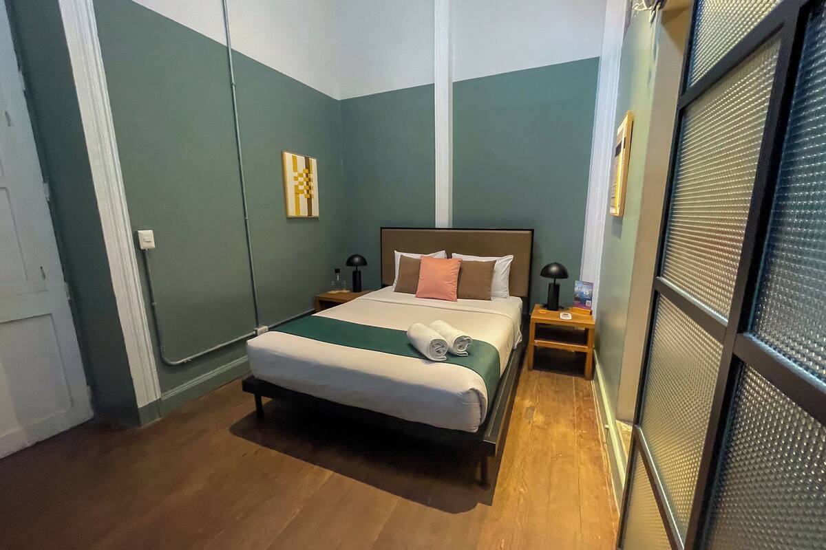 A neatly arranged bedroom with a bed, bedside tables, and a window with blinds.
