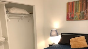 Et soveværelse med seng, natbord, lampe, et billede og et skab.