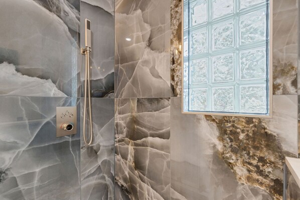A bathroom with marble walls, a shower, and a frosted glass window. - Seagrass Escape - Monthly Beach Rental (Clearwater Beach)