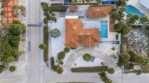 Vue aérienne d’une propriété dotée d’une piscine, d’un patio couvert et d’une route avec un trottoir.