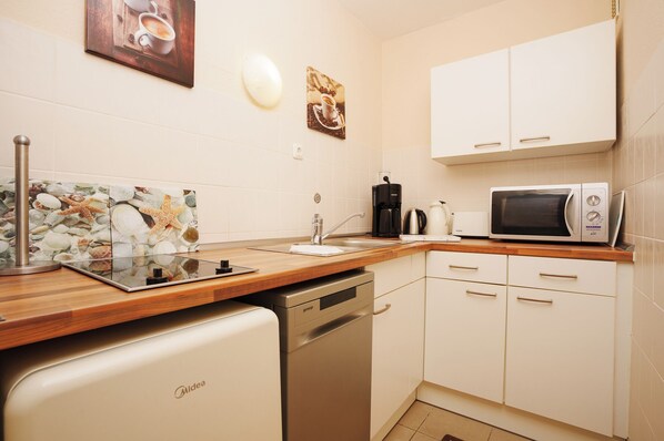 A compact kitchen with white cabinets, a microwave, a coffee maker, and a dishwasher.