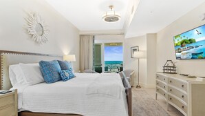 A bedroom with a bed, bedside tables, a dresser, a TV, and a view of the ocean.