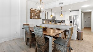 A modern kitchen with white cabinets, a wooden dining table, wicker chairs, and pendant lighting. - BEACHFRONT l PRIVATE BEACH l BEACH SET UP INCLUDED l STUNNING WATER VIEWS (Santa Rosa Beach)