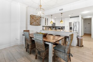 A modern kitchen with white cabinets, a wooden dining table, wicker chairs, and pendant lighting. - BEACHFRONT l PRIVATE BEACH l BEACH SET UP INCLUDED l STUNNING WATER VIEWS (Santa Rosa Beach)