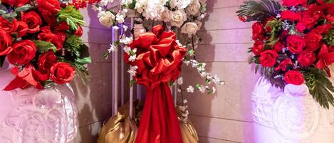 A floral arrangement with red and white flowers, a golden statue, and a red cloth draped over it.