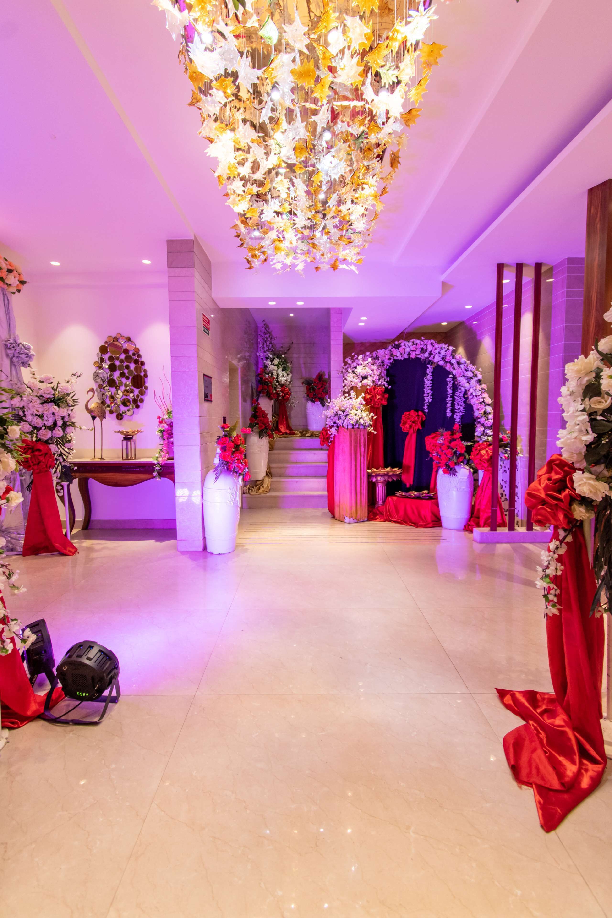 Un pasillo bien iluminado con un candelabro, adornos florales y una escalera que conduce a un área decorada.
