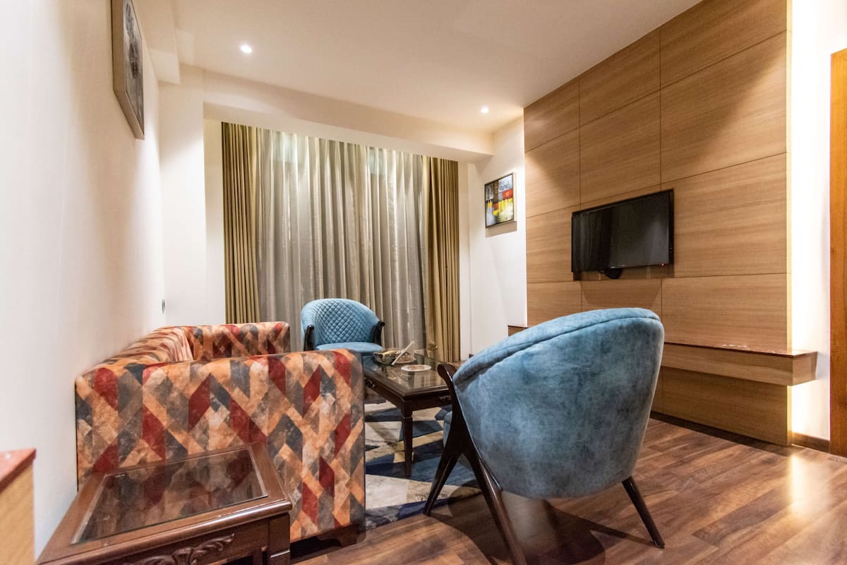 A modern living room with a sofa, a blue armchair, a glass coffee table, and a flat-screen TV mounted on a wooden wall.