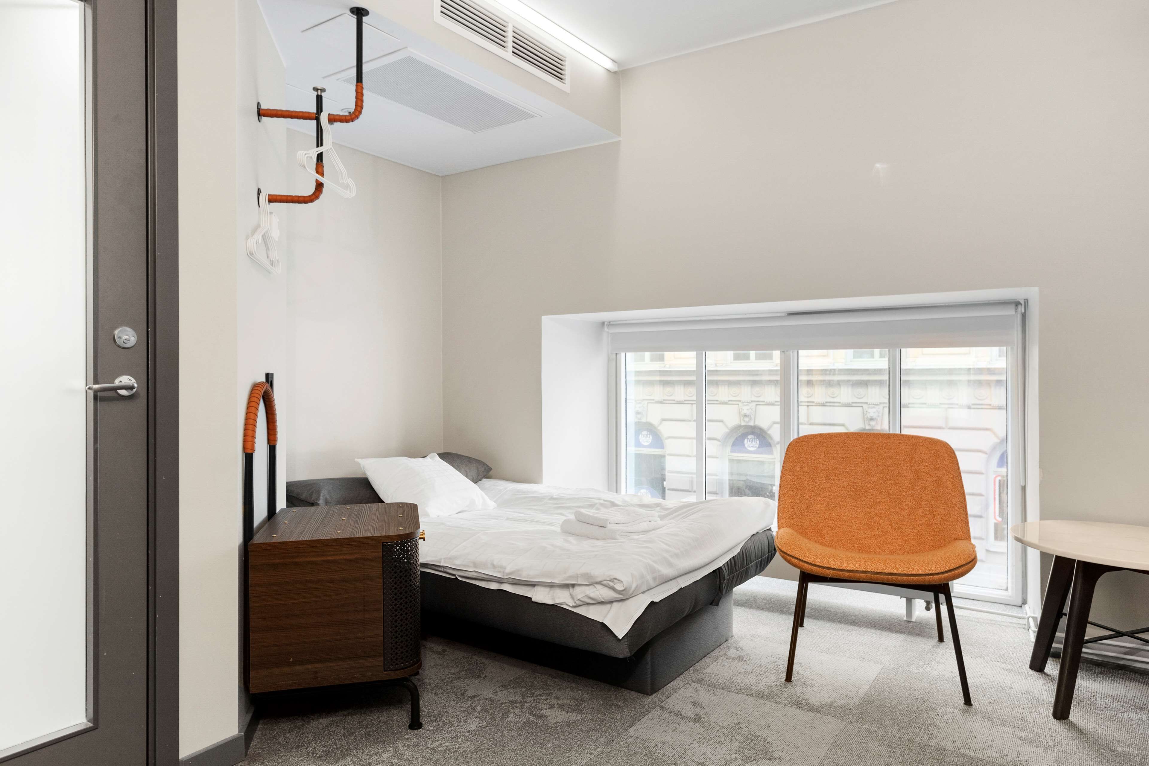 A bedroom with a bed, a chair, a small table, and a window.