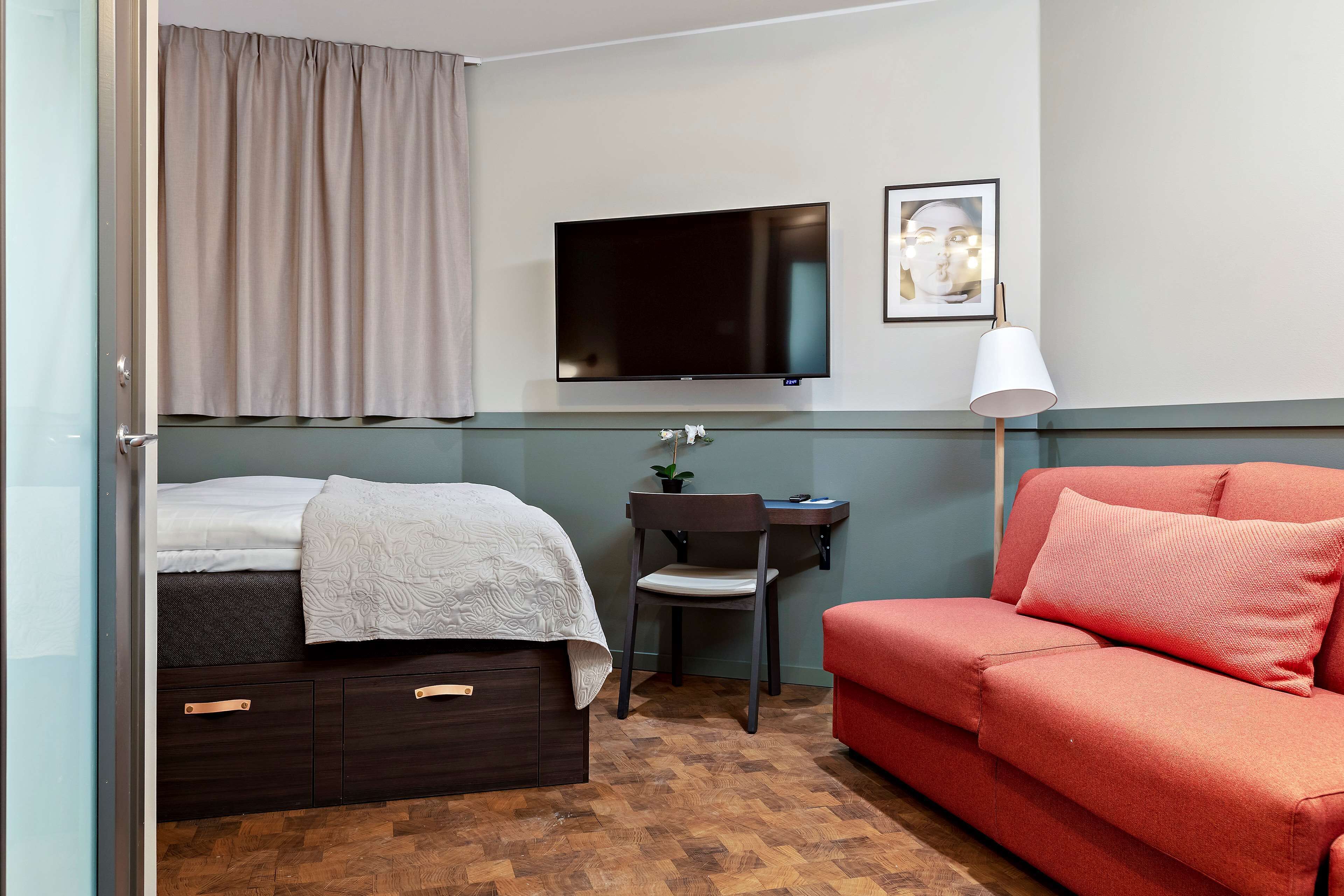 Una habitación de hotel con cama, escritorio, televisión, sofá rojo y una silla.