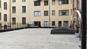 Un patio con piso empedrado, cerca de metal y un edificio con múltiples ventanas y balcones.