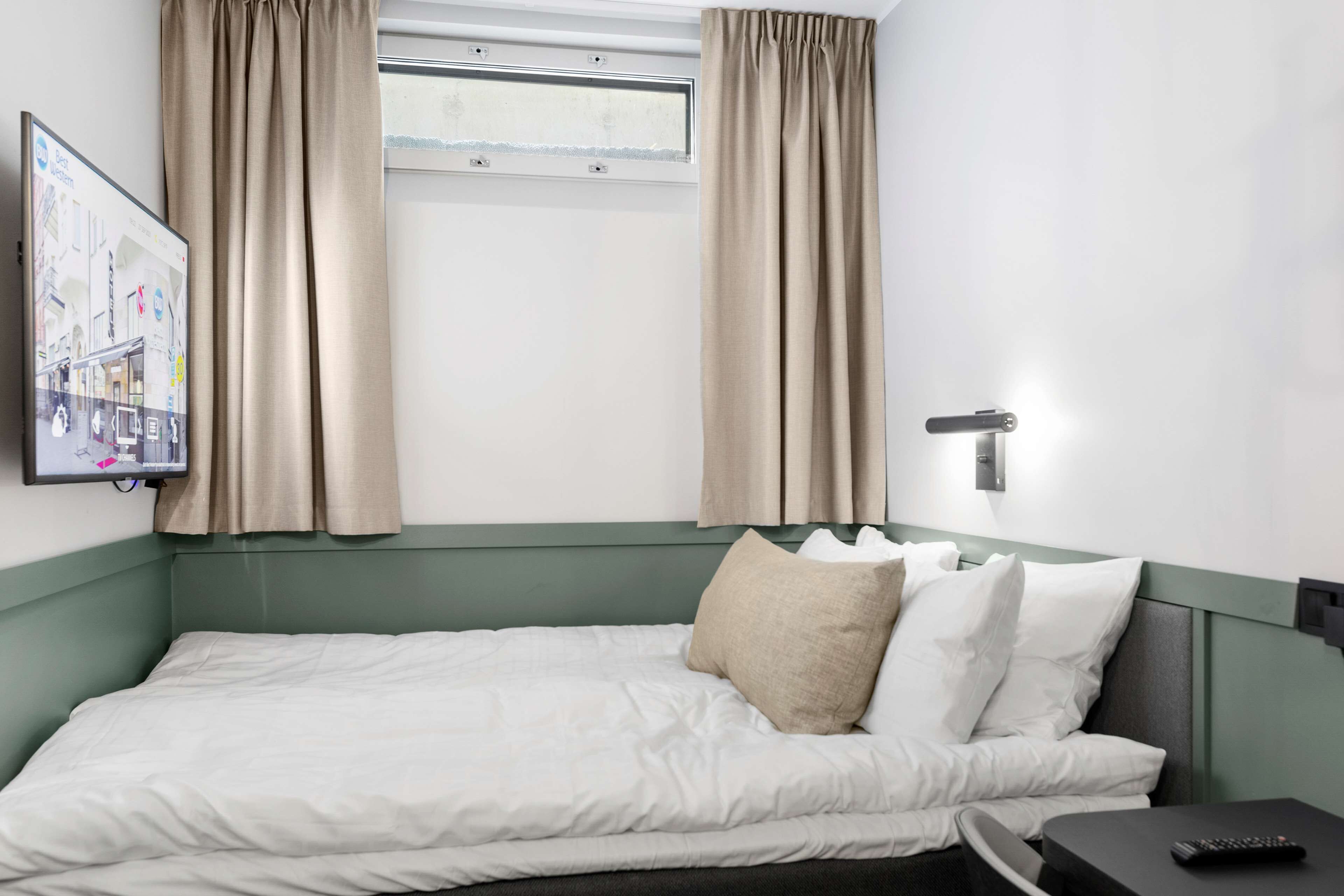 A hotel room with a bed, a nightstand, a remote control, and a window with curtains.