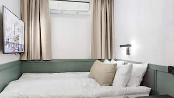 Een hotelkamer met een bed, nachtkastje, afstandsbediening en een raam met gordijnen.