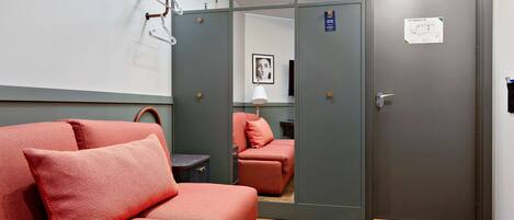 Habitación de hotel con sofá, espejo, puerta con un cartel y suelo de madera.