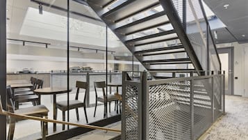 A modern interior with a staircase, glass partitions, and seating areas.