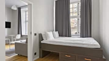 A modern bedroom with a bed, grey curtains, a small desk, and a chair.