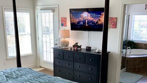 Un dormitorio con una cama grande, un aparador, un televisor y un baño visible a través de una puerta abierta.