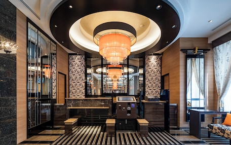 A modern lobby with a central chandelier, check-in counters, and a patterned wall design.