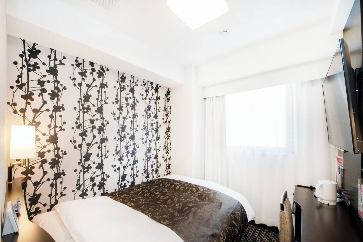 Une chambre d’hôtel avec un grand lit, un bureau avec une machine à café, une télévision et une fenêtre avec des rideaux.